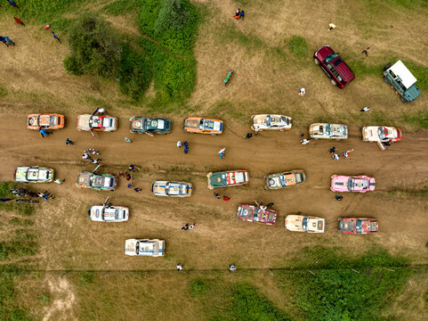Aerial view of off-road vehicles racing on a dirt road surrounded by scenic grasslands and people in an outdoor event, Mbirikani, Kenya.