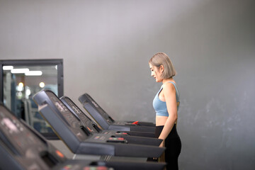 Fototapeta premium fitness asian exercise woman running device treadmill. healthy fitness trainer jogging on treadmill to exercise legs muscle. adult woman running treadmill burn fat and calories on electric equipment