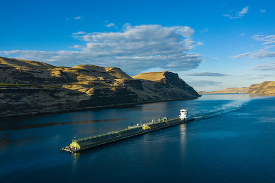 Aerial view of serene river barge and tugboat navigating the tranquil Columbia River Gorge surrounded by majestic mountains, Benton County, United States.