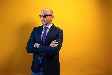 A man in a suit and sunglasses is standing in front of a yellow wall.