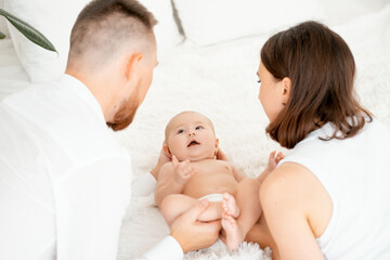 mom, dad with a baby, an international family, a Caucasian mom with an Asian husband and a baby in her arms in the bedroom gently hugs the baby holding in her arms, a place for text