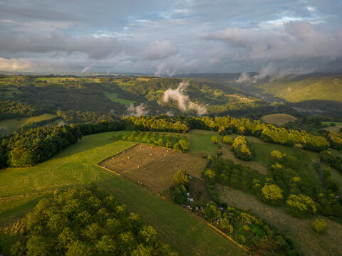 Aerial view of picturesque rolling hills and lush fields under a golden hour sky with clouds, Chenailler-Mascheix, France.