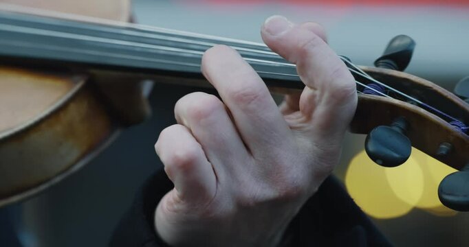 Man is playing a violin on public street at Christmas market. Concept of elegance and sophistication, as the person's hand skillfully moves the bow across the strings