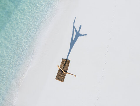 Aerial view of a serene beach with a woman practicing yoga on a mat, surrounded by clear turquoise waters and gentle waves, Thoddoo, Maldives.