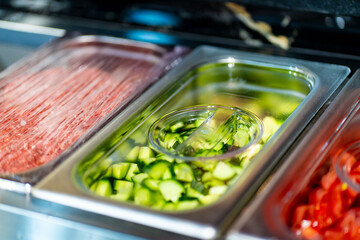Metal containers filled with various sliced vegetables and ingredients in a professional kitchen setting