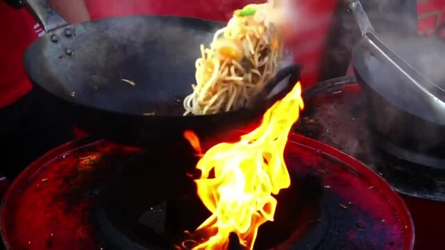Street-side wok fire in slow motion. Slowmo cook fires up hot oil with vegetables outside on the road at night in downtown. chef cooking delicious fried noodles