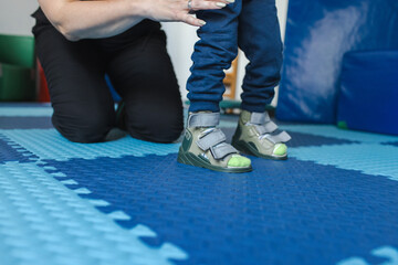 Physiotherapist supports a young boy with cerebral palsy as he practices walking in a...