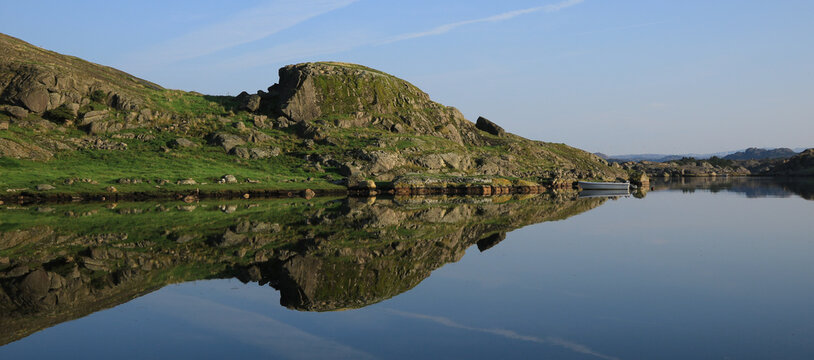Rock formations and fishing boat reflecting in a bay of the North sea in Rogaland, Norway.