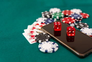 close up of Smartphone with red dice, poker cards and casino chips on green felt background