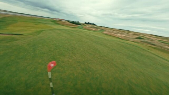 FPV drone fly around putting green on rolling green par 5 of coastal Ireland links golf course