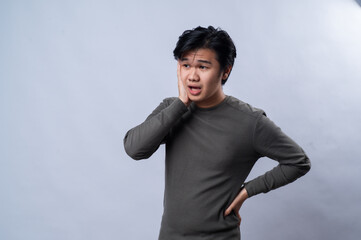 An Asian man is leaning on one hand with a bored or tired expression, slightly pouting, wearing a...