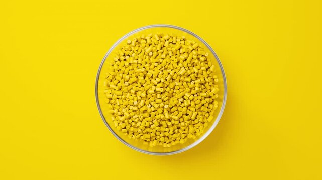 Rotating glass bowl with yellow plastic polypropylene granules, masterbatch polymer grain on yellow backdrop. HDPE or PVC resin pellets. 3d render animation