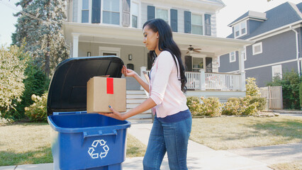 Woman Putting Cardboard Into Recycling Bin On Suburban Street