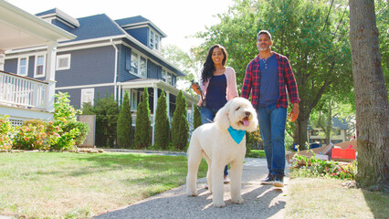 Low Angle Shot Of Couple Walking Dog Along Suburban Street