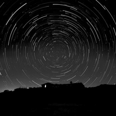 Fototapeta premium Cosmic Dance Long Exposure of Star Trails Circling Above a Solitary House on the Horizon.