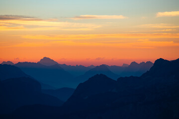 Distant mountain peaks layers at sunrise. Pattern of mountains silhouettes against orange sky in Dolomites.