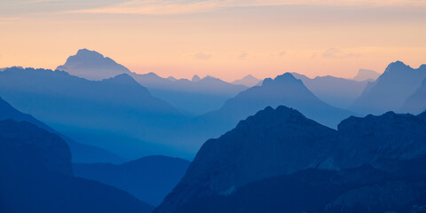 Distant mountain peaks layers at sunrise. Pattern of mountains silhouettes against orange sky in Dolomites.