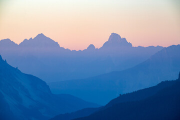 Distant mountain peaks layers at sunrise. Pattern of mountains silhouettes against orange sky in Dolomites.