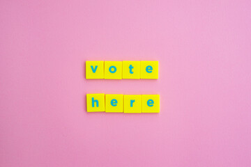'Vote here' political statement with blue letter, yellow squares on pink paper 