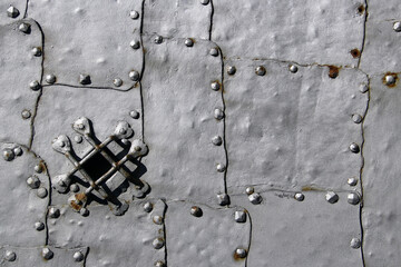 A detailed view of an old castle entrance gate, clad in metal, adorned with rivets, with a small inspection window or peephole.