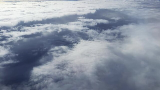 Plane flight timelapse or hyper lapse over sky is filled with clouds, creating a moody atmosphere. The clouds are white and fluffy, giving the sky a sense of calmness and serenity