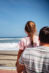 A father embraces his daughter, creating a moment of warmth and connection as they stand by the ocean