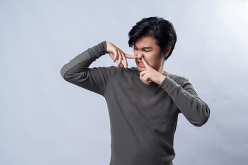 An Asian man in a gray long-sleeved shirt makes a disgusted expression while covering his mouth and...