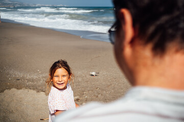 A father spends quality time with his daughter by the ocean, sharing a relaxed and joyful day at the beach