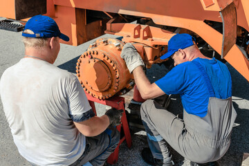 Two mechanics collaborate on machinery repair, both equipped with uniforms and gloves, working...