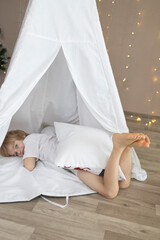 barefoot boy lies in a white wigwam tent. cozy rest in the children's room. childhood, comfort at home. Selective focus on feet © Anna
