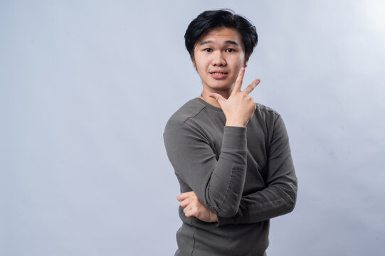 Portrait of an Asian person wearing a long-sleeved gray shirt, showing a specific number with their fingers, isolated against a white background.