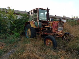 Old rusty tractor in the yard under the open sky. Old non-working destroyed equipment. Agriculture...