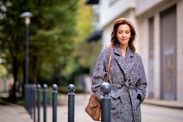 Attractive mid aged woman walking outdoors in city street on autumn day