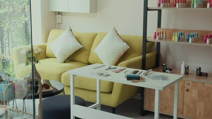 Medium long shot of interior of modern nail art studio with yellow sofa positioned next to table with various tools in manicure salon