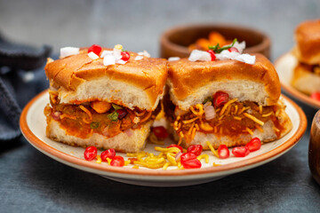 Dabeli is a spicy Indian street food made with a potato filling, tamarind chutney, and sev, served in a bun.
