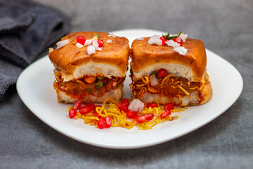 Dabeli is a spicy Indian street food made with a potato filling, tamarind chutney, and sev, served in a bun.
