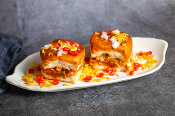 Dabeli is a spicy Indian street food made with a potato filling, tamarind chutney, and sev, served in a bun.