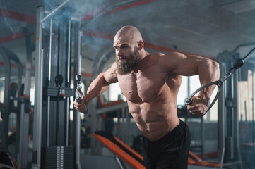 Bald Caucasian bodybuilder training chest using cable crossover in gym. 