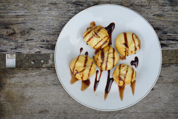 Several delicious profiteroles made of light choux pastry are arranged on a white plate drizzled generously with chocolate sauce.