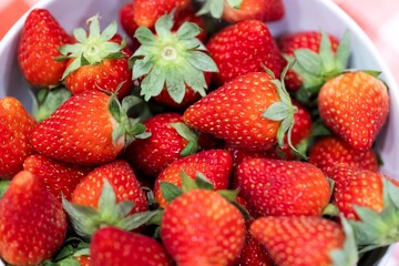 A portrait of a bunch of red tasty fresh strawberies with the green top in a white bowl. The delicious fruit is ready to be eaten.
