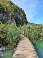 A girl walks along a wooden path through the scenic beauty of Plitvice Lakes National Park, Croatia, surrounded by nature