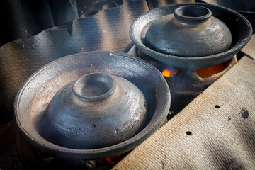 Fototapeta premium A row of traditional clay pots, used for cooking the Indonesian pancake Serabi, is heated over a charcoal fire in an authentic kitchen. Culinary heritage concept
