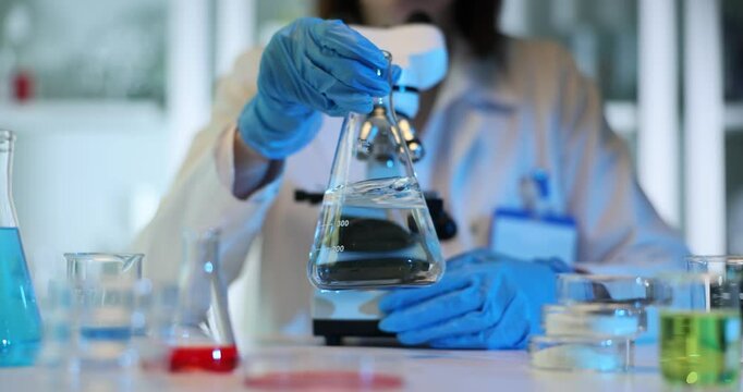 Scientist holds in hands flask with transparent liquid in laboratory