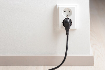 A close-up of a double electrical outlet mounted on a white wall, with a power cord plugged into one of the sockets
