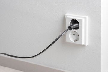 A close-up of a double electrical outlet mounted on a white wall, with a power cord plugged into one of the sockets