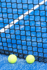 view of the net of a blue paddle tennis court and two balls , concept of racket sports