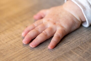 A portrait of the small hand of a cute baby lying on a wooden floor while it is crawling. The tiny fingers of the newborn are all flat on the surface.