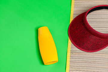 Jar of sunscreen and visor on top of straw mat on green background. Summer concept. Sun protection concept. copy space.