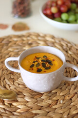 Pumpkin and potato creamy soup, bowl of grapes, jars of nuts and autumn leaves on the table. Selective focus.