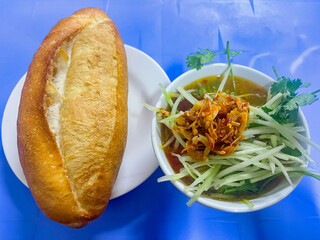 Dalat style pork meatball Banh Mi with dipping sauce including meatballs, shredded spinach and topped with stir-fried chili and fried onions